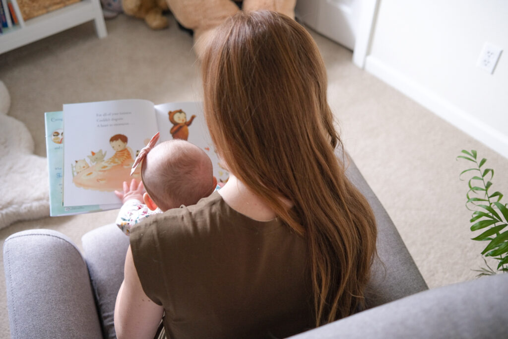 Picture of a mother and baby reading a book in a chair. The picture is taken from behind looking down at the book.